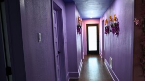 Käytävä, jonka seinät ovat violetit ja jossa on puulattia, johtaa valoisaan oviaukkoon.