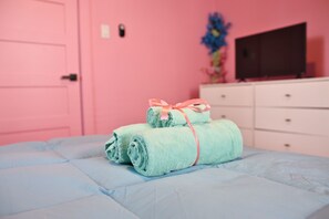 Ein Bett mit aufgerollten Handtüchern und einer rosafarbenen Wand.