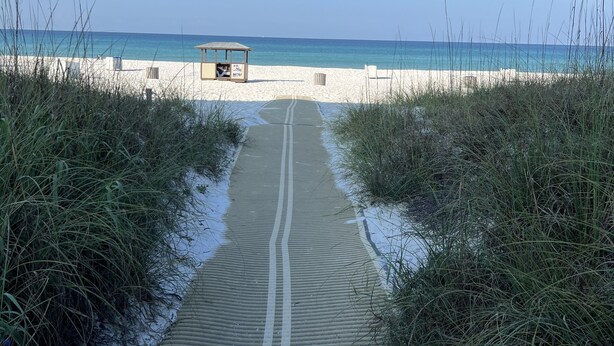 Un sentier qui longe la plage et mène à une zone de plage où se trouve une petite construction.