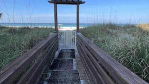 Une promenade en bois menant à une plage, avec une structure en forme de pergola.