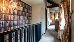 Un pasillo con una estantería llena de libros, un candelabro y una escalera que lleva a otra habitación.