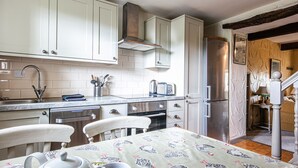 A kitchen with white cabinets, a stainless steel refrigerator, and a dining table with a patterned tablecloth. - Cuckoo (Bakewell)