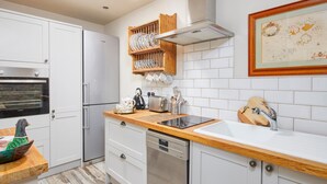 A modern kitchen with white cabinetry, a built-in oven, a dishwasher, and a wooden countertop. - Love Nest (Bakewell)