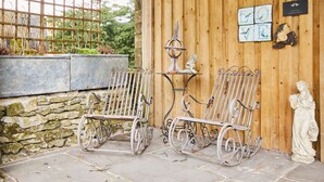 A rustic outdoor seating area with wrought iron chairs and a stone wall backdrop. - Love Nest (Bakewell)