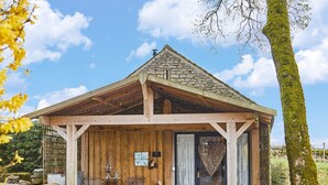 A rustic wooden building with a stone roof, a bench, and a statue in front. - Love Nest (Bakewell)