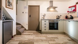 Una cocina con horno empotrado, estufa y lavamanos. Una escalera conduce a otro nivel.