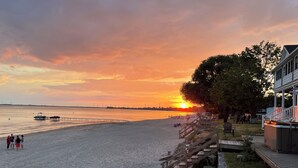 A beach with a wooden staircase leading to a building, a boat on the water, and a sunset in the background. - Sunset Getaway on Long Beach (Wainfleet)