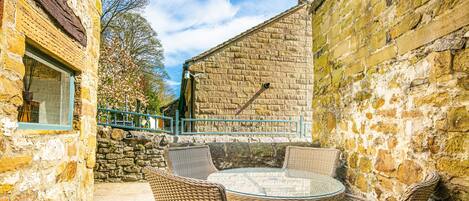 A stone building with a glass table and wicker chairs in a courtyard.