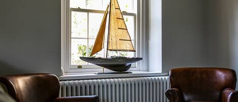 A room with a large window, a model sailboat on a windowsill, and two leather chairs.