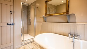 Un baño con ducha a ras de suelo, bañera y espejo con marco decorativo.