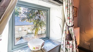 Una ventana con vistas a un árbol y un edificio, un radiador blanco y una cortina con estampado floral.