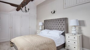 A bedroom with a large bed, white nightstands, a chandelier, and built-in wardrobes. - The Dower House (Bakewell)