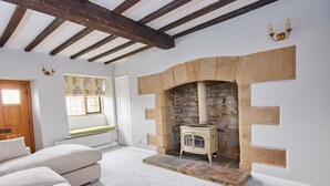 A room with a stone fireplace, a wooden ceiling, a window with a view, and a sofa. - The Dower House (Bakewell)