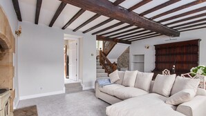 A spacious living room with a large beige sectional sofa, a wooden staircase, and a stone wall. - The Dower House (Bakewell)