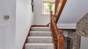 A staircase with a wooden handrail and carpeted steps, leading to a room with a stone wall and a window. - The Dower House (Bakewell)