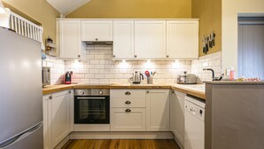 Una cocina con armarios blancos, encimera de madera, horno, lavavajillas y refrigerador.