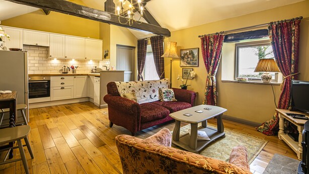 Una sala de estar acogedora con sofá, sillón y mesa de centro, una cocina con armarios blancos, y un comedor con mesa y sillas.