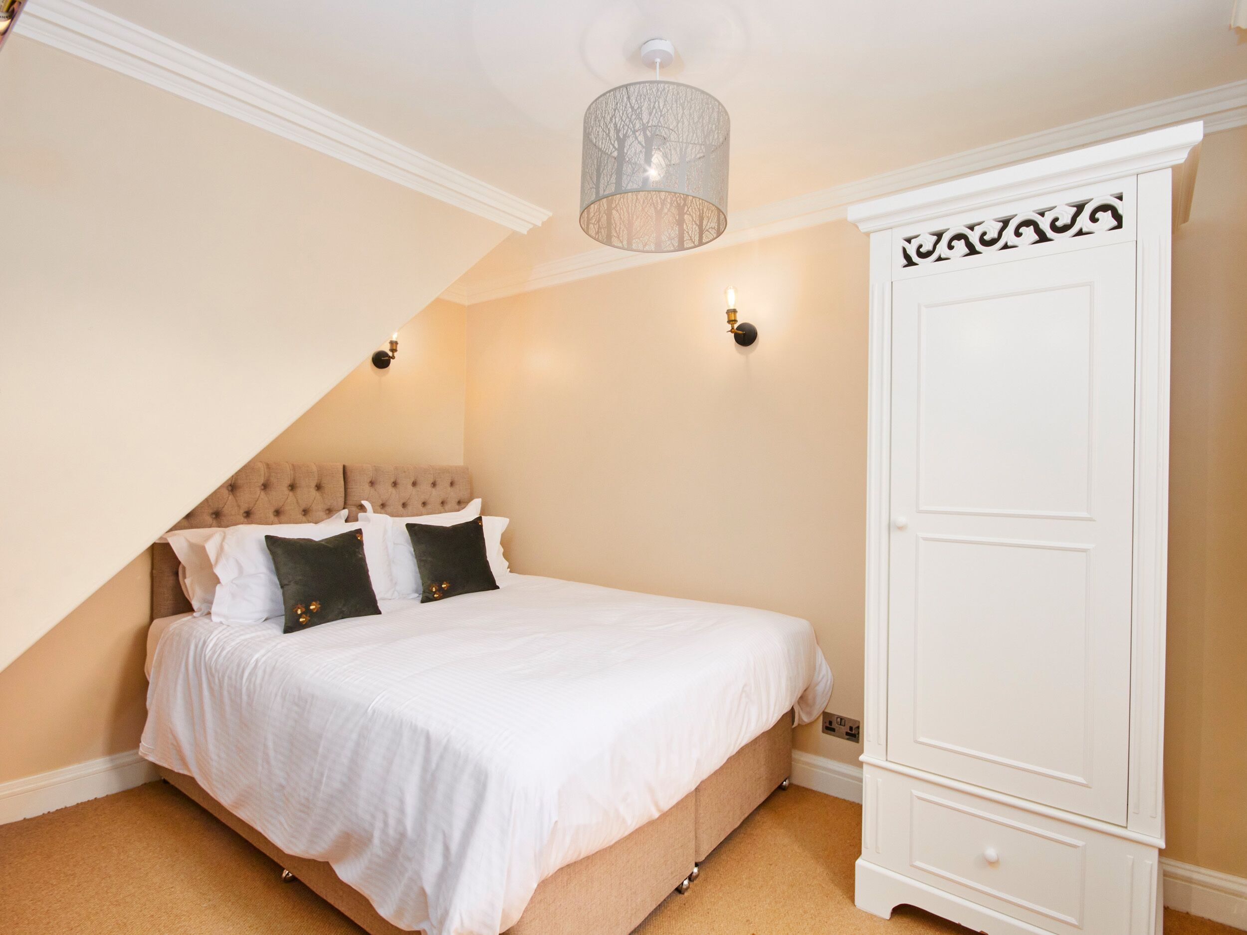 A bedroom with a large bed, a white wardrobe, and a hanging light fixture.