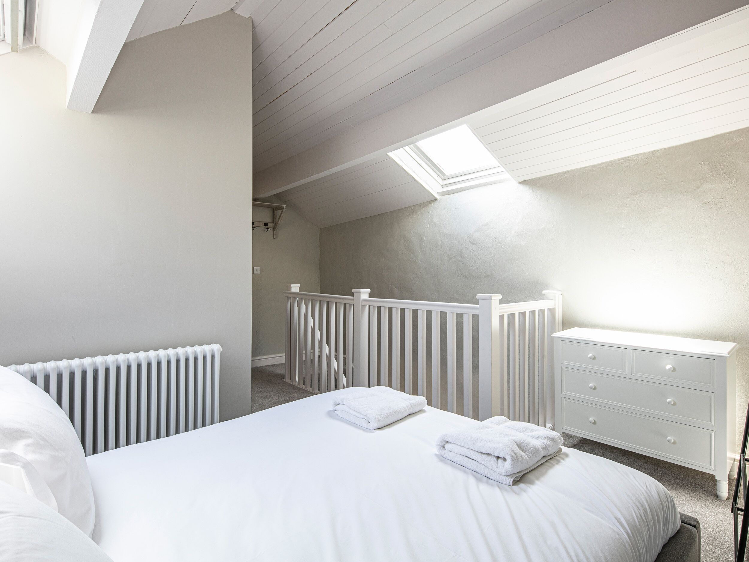 A bedroom with a bed, a dresser, a radiator, and a skylight.
