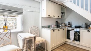 A modern kitchen with wooden flooring, white cabinets, a built-in oven, and a window with a view of a stone wall. - The Artists Loft (Bakewell)