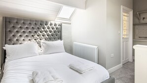A bedroom with a tufted headboard, white bedding, a radiator, and a skylight. - The Artists Loft (Bakewell)