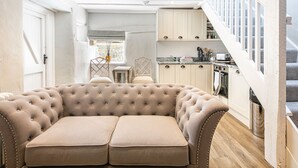 A cozy living room with a tufted sofa, a kitchen with white cabinets, and a staircase. - The Artists Loft (Bakewell)