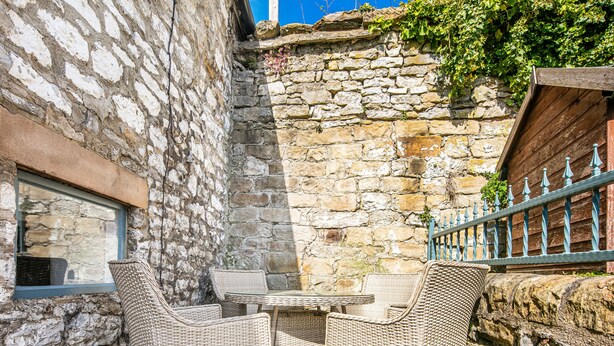 A stone-walled outdoor seating area with wicker furniture. - The Artists Loft (Bakewell)