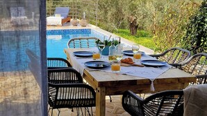 A dining table set for four with a pool view, surrounded by stone flooring and black chairs.