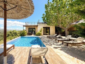 A modern outdoor pool area with lounge chairs and a thatched umbrella. - Fantastic sea view villa with heated pool & roof terrace | 6 guests (Kamilari)