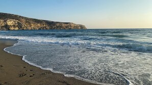 A beach with waves crashing onto the shore, a rocky cliff in the background, and a clear sky.