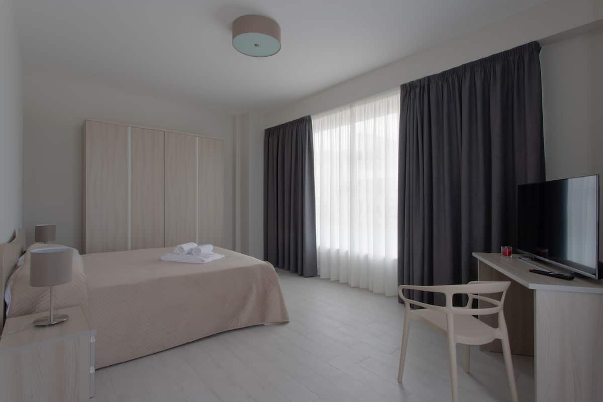Habitación de hotel con cama, escritorio con televisor, silla y ventana con cortinas.
