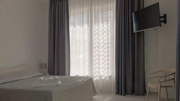 Une chambre d’hôtel moderne, équipée d’un lit, d’un téléviseur fixé au mur, d’une chaise et d’une fenêtre avec des rideaux.