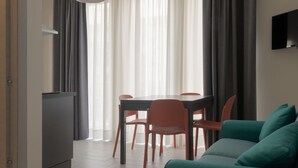 Un salon moderne avec un canapé de couleur turquoise, une table à manger avec des chaises rouges et un téléviseur à écran plat fixé au mur.