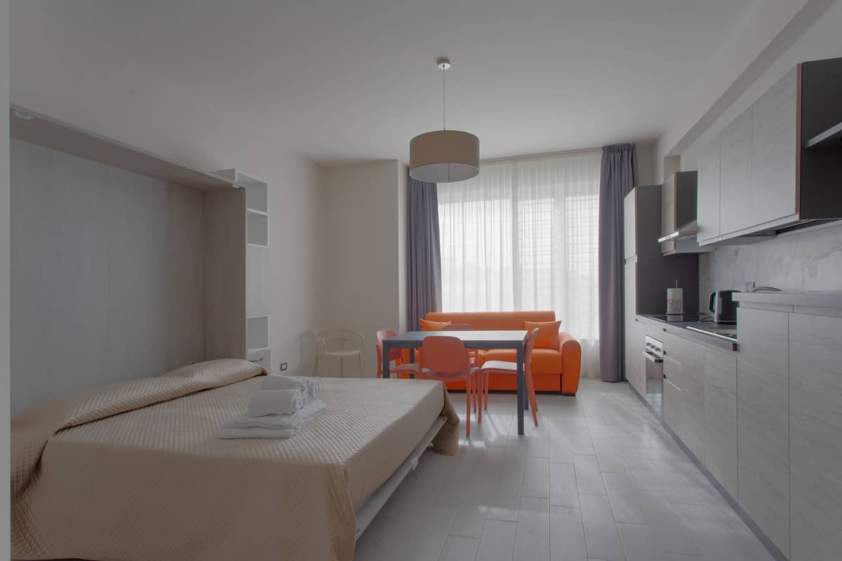 Una habitación de hotel moderna con cama, una mesa de comedor con sillas, un sofá y una zona de cocina.