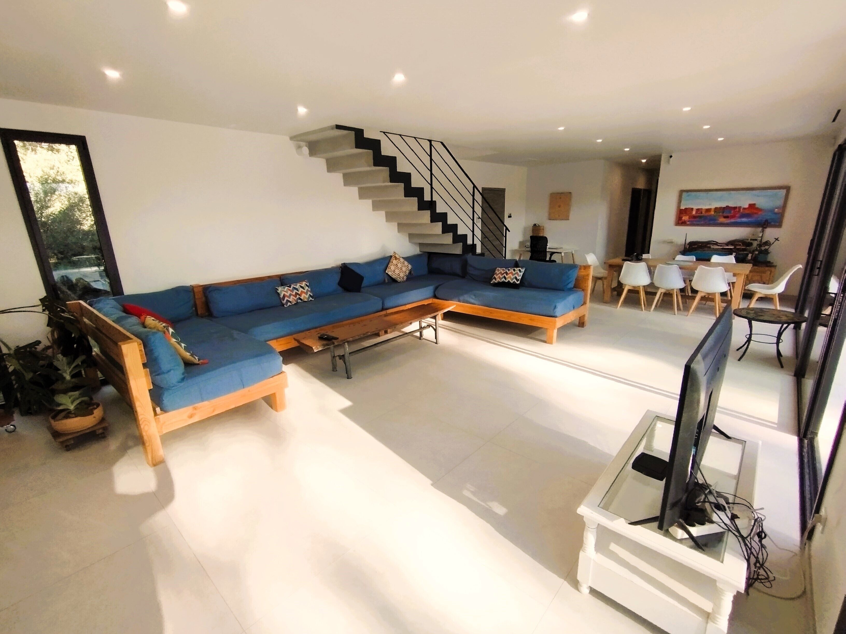Ein modernes Wohnzimmer mit einem blauen Modulsessel, einem Holztisch, einem Fernsehschrank und einer Treppe.