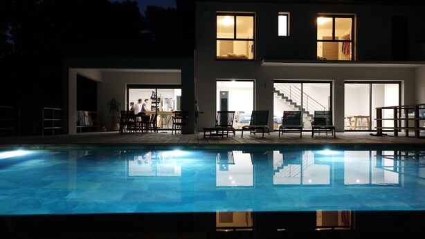 Una casa moderna con piscina, ventanas amplias y una escalera que sube al piso superior.
