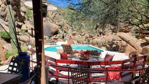 A poolside area with a round table and chairs, surrounded by a wooden fence.