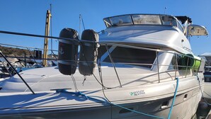 A white yacht docked at a marina with a visible registration number and a green hose coiled on the deck.