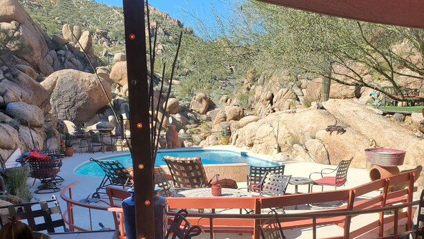 An outdoor patio with tables and chairs, a pool, and a rocky landscape in the background.