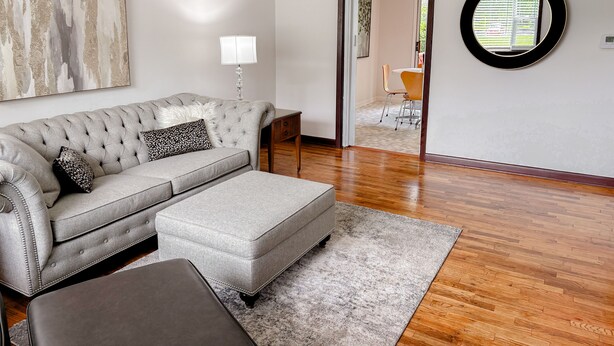 A living room with a grey sofa, a matching ottoman, a round mirror, and a painting on the wall. - Good Vibes House - Centrally located, cozy house!  (Springfield)