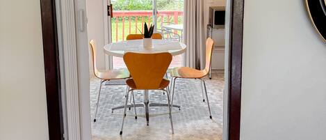 A doorway leading to a dining area with a round table and orange chairs, a ceiling light fixture, and a view of a balcony with a red railing.