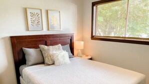 A neatly made bed with a white comforter and pillows, a wooden headboard, and a bedside table with a lamp. There are two framed leaf designs on the wall above the bed. - Good Vibes House - Centrally located, cozy house!  (Springfield)