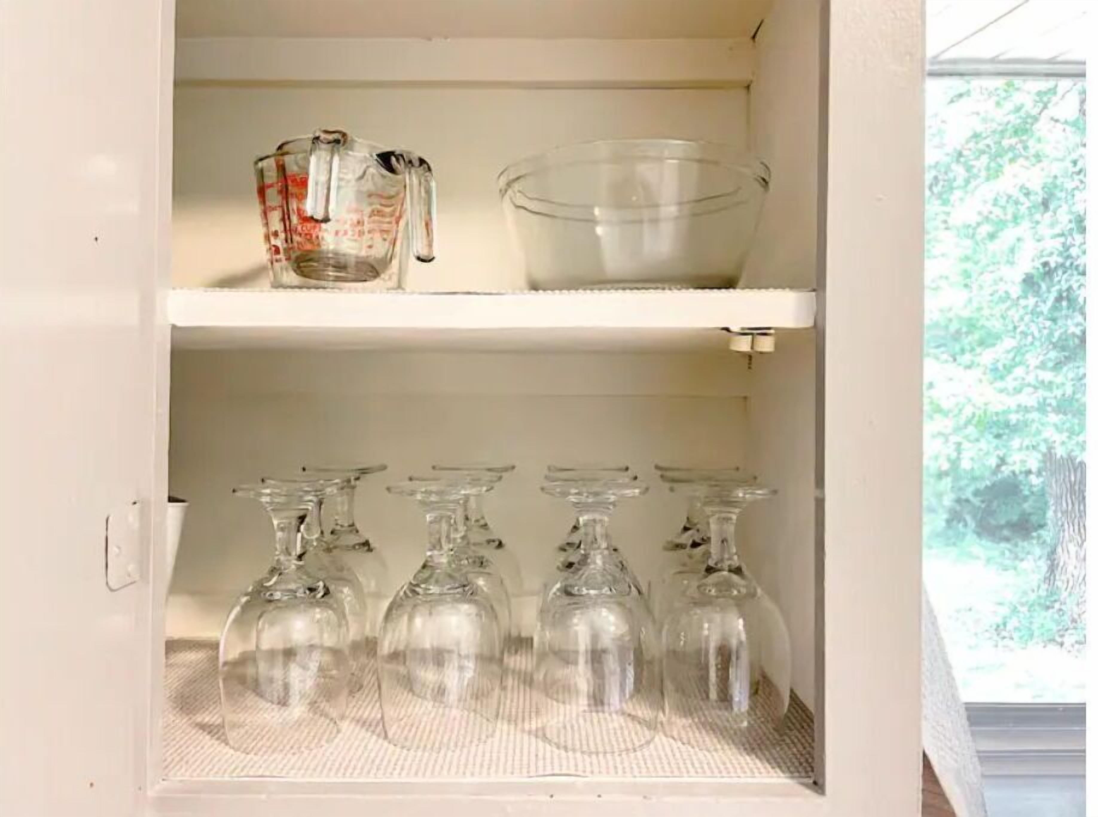 A kitchen cabinet with shelves holding a measuring cup, a mixing bowl, and several wine glasses.