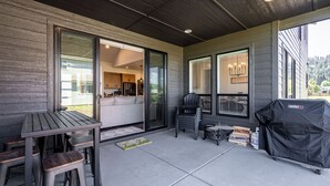 A covered patio area with a table and chairs, a grill, and a sliding glass door leading to a kitchen.