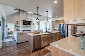 Une cuisine moderne dotée d’un îlot central, de meubles en bois, d’appareils électroménagers en acier inoxydable et de luminaires suspendus.