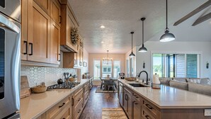A modern kitchen with wooden cabinets, a central island, pendant lighting, and a view to the dining area.