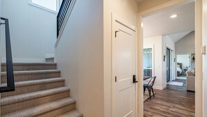 A staircase leading to a landing with a white door, a wooden floor, and a view into a living area with a sofa and a dining table.