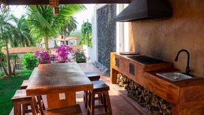 An outdoor kitchen with a long wooden table and stools, a stone wall, and a sink. - Wonderful residence w/studio, 15 min walk distance from beach & restaurants! (Ixtapa Zihuatanejo)