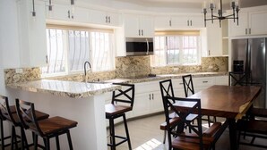 A modern kitchen with white cabinets, granite countertops, and a central island with bar stools. - Wonderful residence w/studio, 15 min walk distance from beach & restaurants! (Ixtapa Zihuatanejo)
