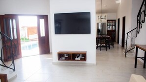 A spacious living area with a flat-screen TV mounted on the wall, a dining table with chairs, and a staircase with a railing. - Wonderful residence w/studio, 15 min walk distance from beach & restaurants! (Ixtapa Zihuatanejo)